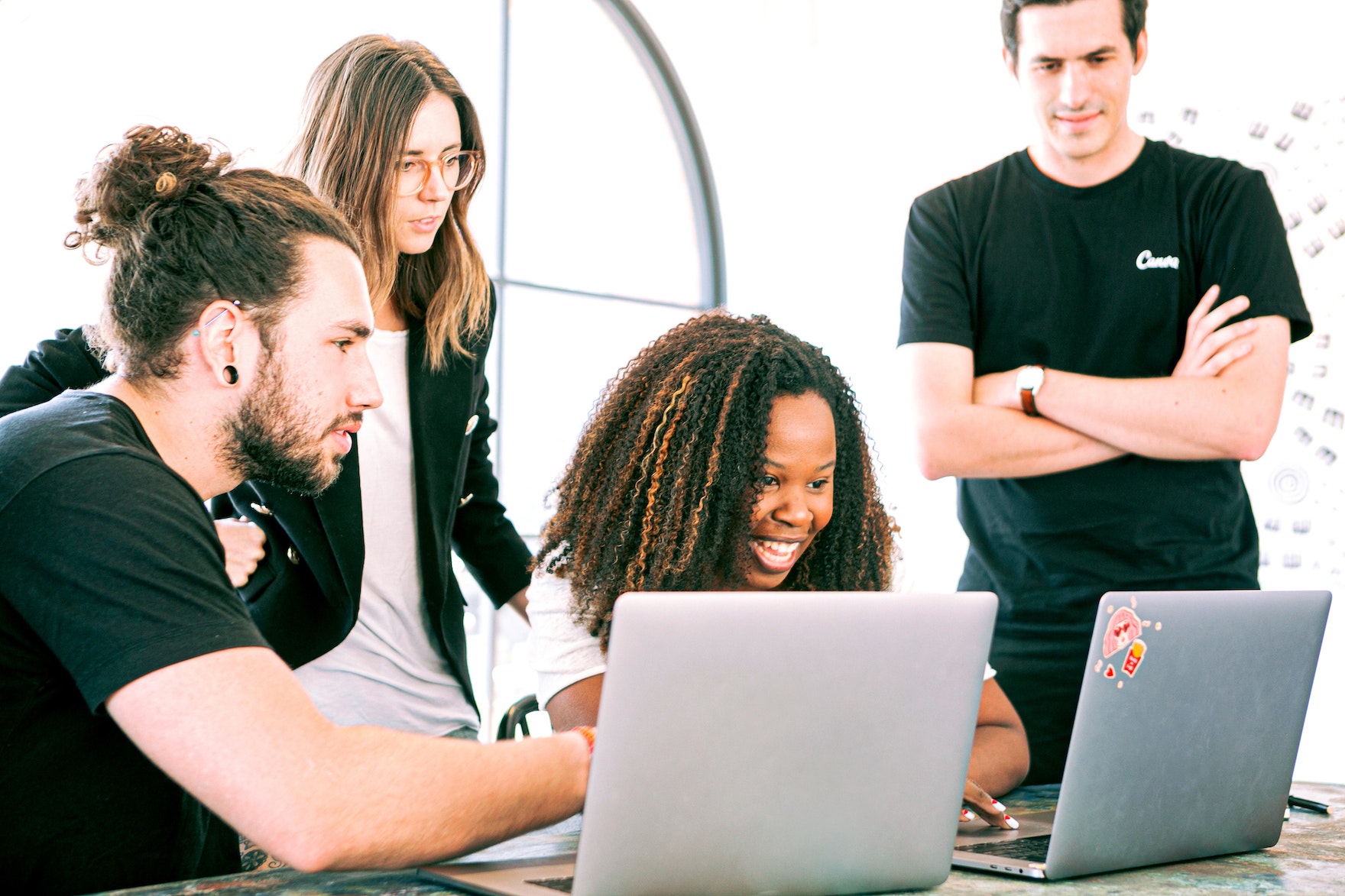 A group of four people sitting and standing behind two laptops collaborating
